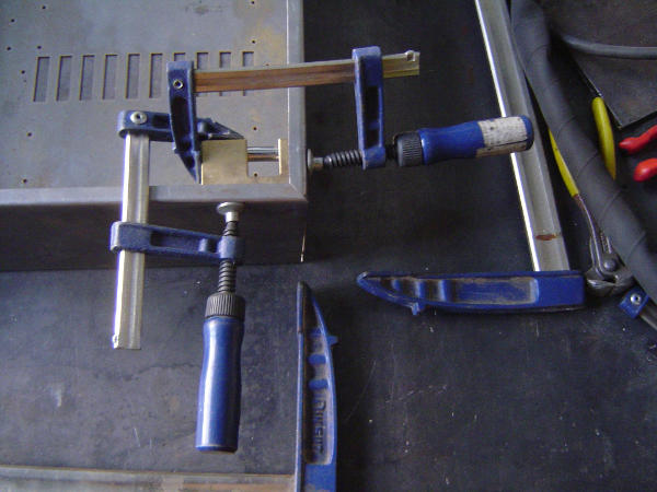 Two clamps holding a brass piece at a corner