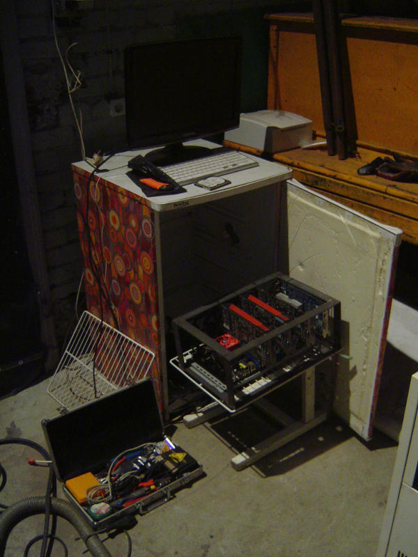 Re-purposed fridge in what looks like a basement, computer mounted in a weded metal strip frame