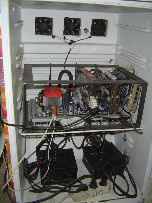Computer on a shelf in the fridge, three fans cut into the fridge back wall above it, two power supply units in the compartment below